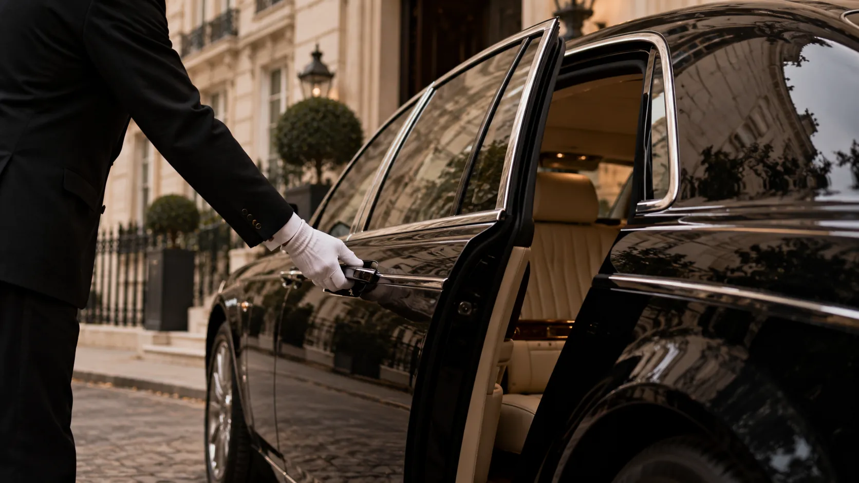 A white-gloved chauffeur opening the door of a black luxury car outside a cream stone townhouse